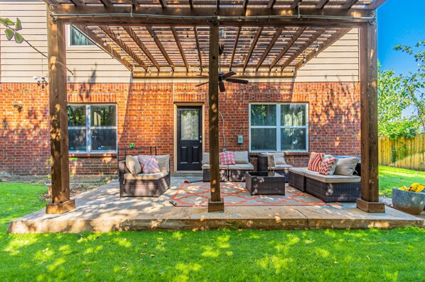 A covered patio with outdoor furniture, a ceiling fan, and a brick house in the background. - Spacious 5BR Dallas Retreat Perfect for Business Travelers Families (Dallas)