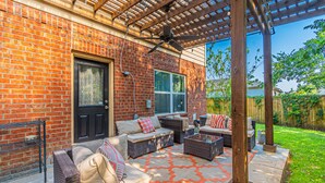A covered patio area with wicker furniture, a ceiling fan, and a brick wall.