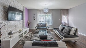 A modern living room with a flat-screen TV mounted on a marble wall, a sofa, a coffee table, and a chandelier.