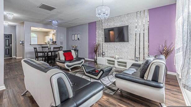 A modern living room with a sofa, coffee table, and TV. There is a dining area with chairs and a table.