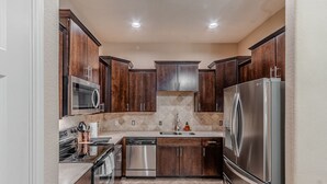 Una cocina compacta con armarios de madera oscura, electrodomésticos de acero inoxidable y un salpicadero de azulejos.