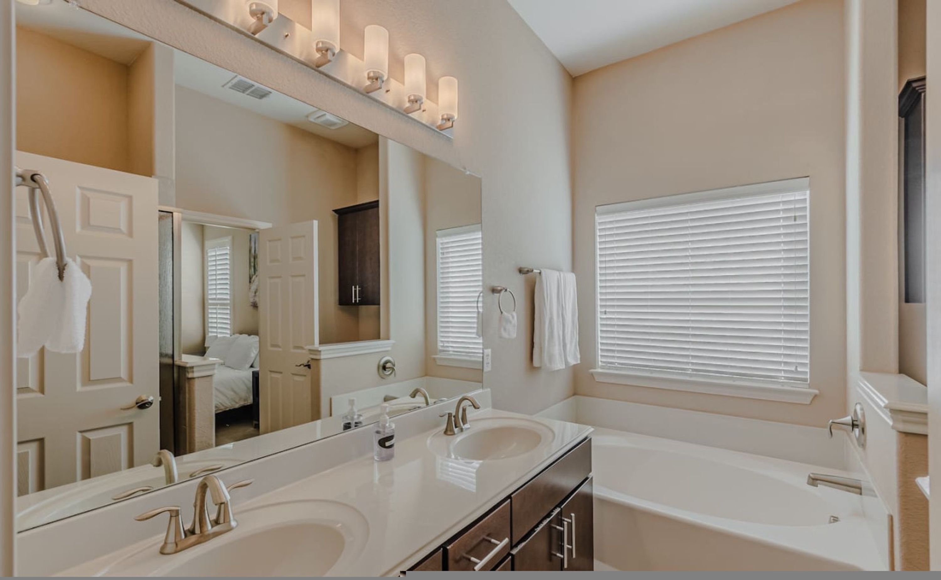 Une salle de bain avec deux lavabos, un grand miroir et une fenêtre avec des stores.