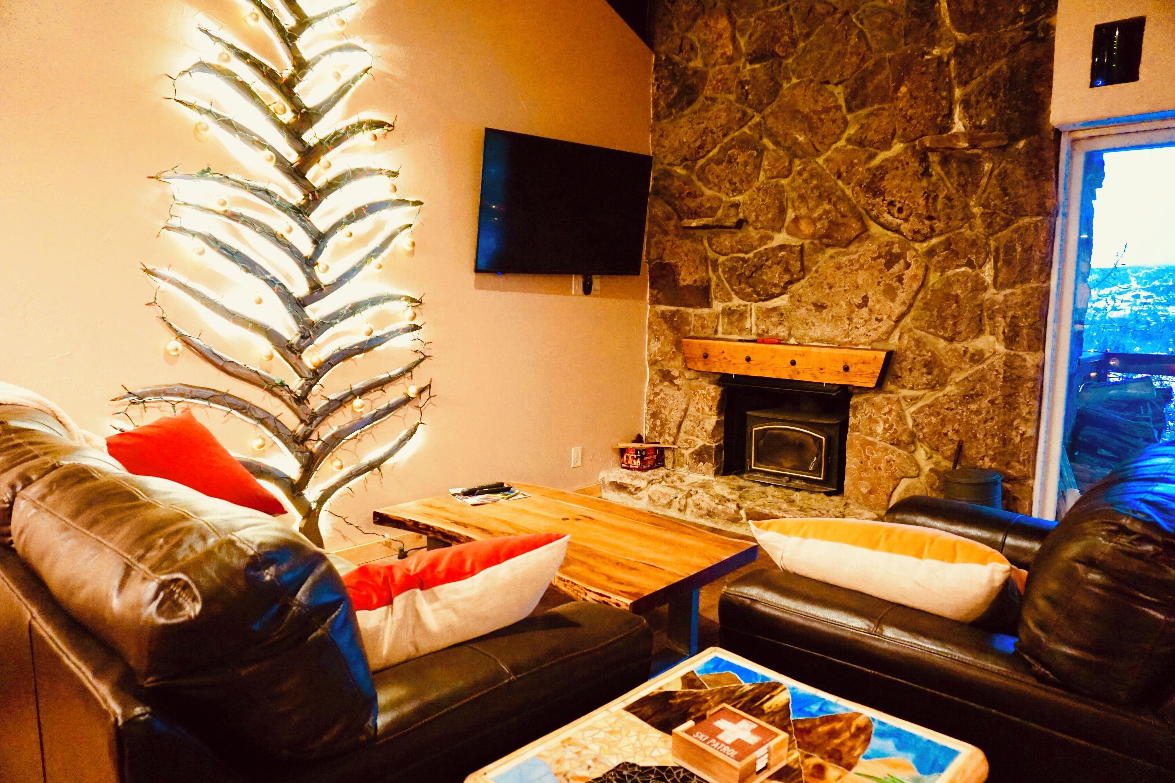 A cozy living room with a stone fireplace, leather sofas, and a flat-screen TV mounted on the wall.