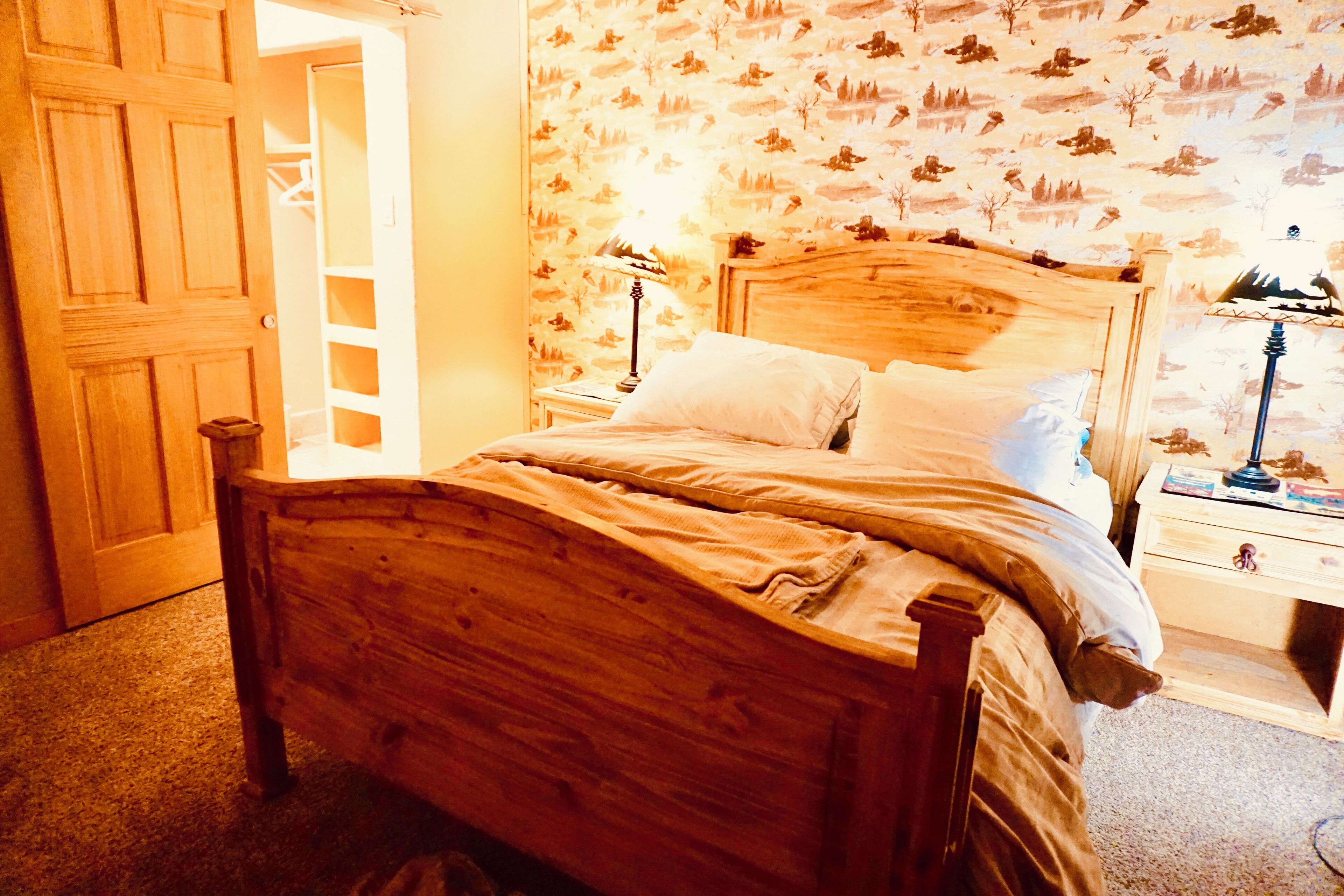 Een houten bed met hoofdeinde, twee nachtkastjes met lampen en een kledingkast.