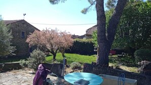 A patio area with outdoor furniture, a stone floor, and a tree with pink blossoms. - Chambres D'hôtes La Magnanerie (Saint-Julien-de-Peyrolas)
