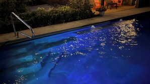 Zwembad met blauwe tint, omgeven door een houten terras en een patio met buitenmeubels.