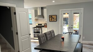 Een moderne keuken met witte kastjes, een groot kookeiland en een eethoek met een lange tafel en stoelen.