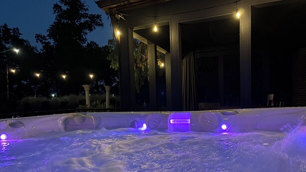 Een bubbelbad met verlichte jets, omgeven door een overdekt terras met zuilen en lichtjes.