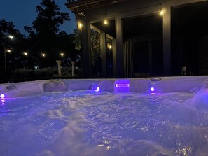 A hot tub with illuminated jets, surrounded by a covered patio area with columns and string lights.