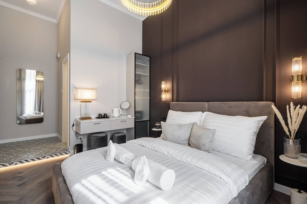 A modern hotel room with a large bed, a desk with a lamp, a mirror, and a wall-mounted light fixture.