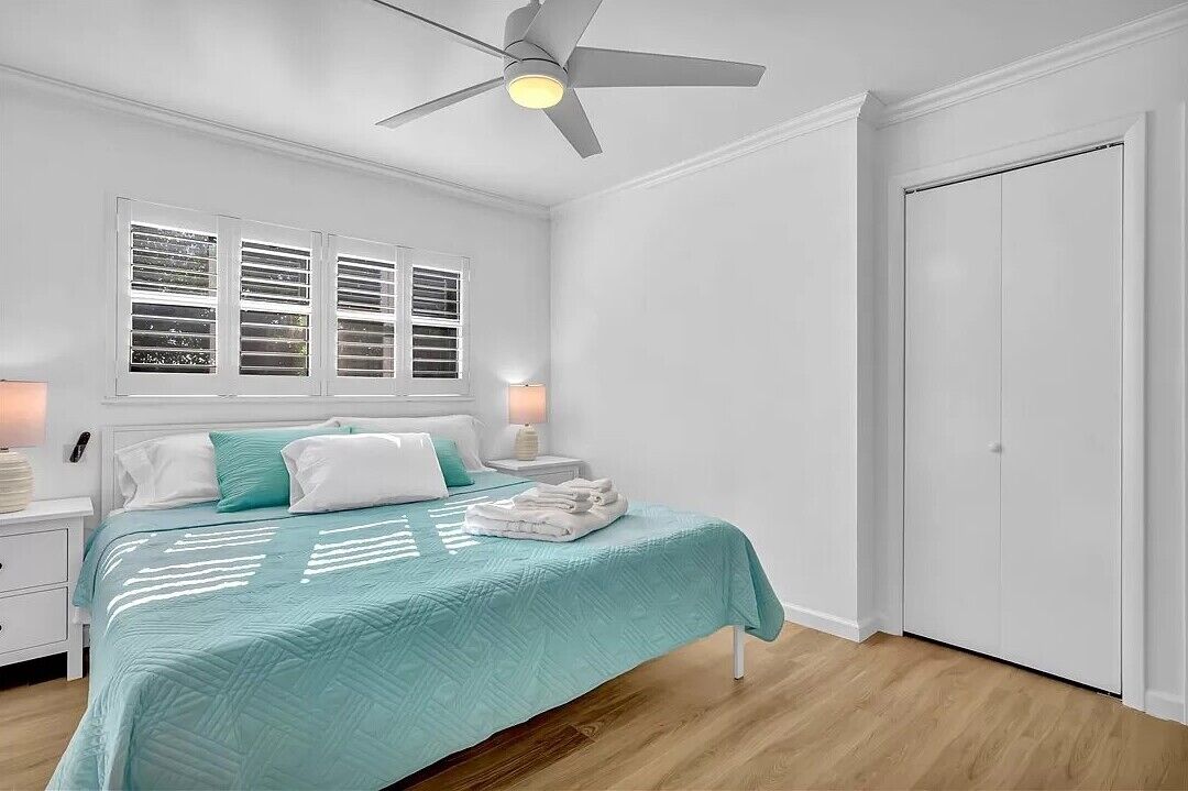 Ein Schlafzimmer mit Bett, Deckenventilator, Fenster mit Jalousien, Nachttisch und Kleiderschrank.