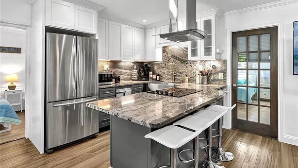 A modern kitchen with white cabinets, a stainless steel refrigerator, a marble countertop, and a large island with bar stools.