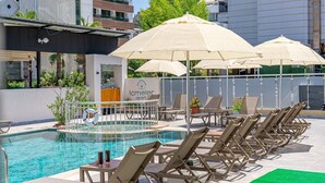 Una piscina con sillas de descanso y sombrillas, rodeada de edificios con balcones.