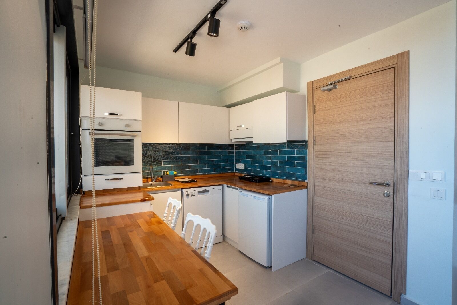 Una cucina compatta con mobili bianchi, un piano di lavoro in legno e uno schienale rivestito di piastrelle blu.