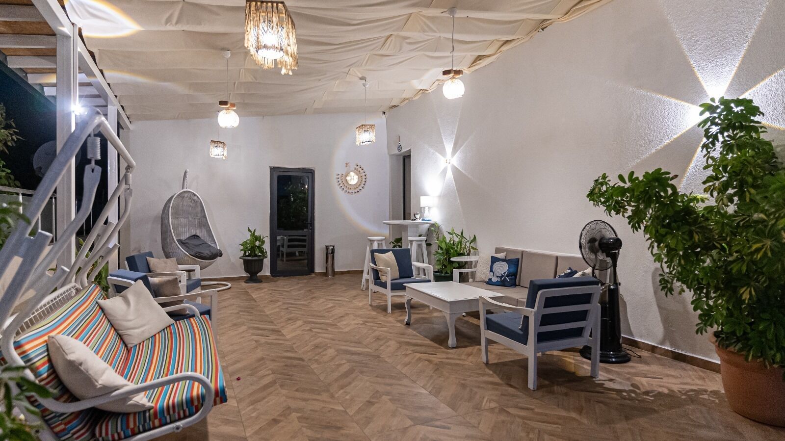 A modern living room with a herringbone floor, white furniture, and a large potted plant.
