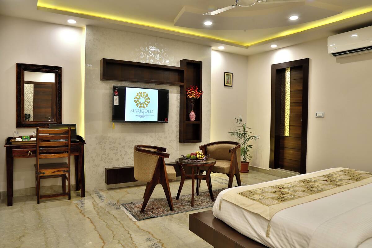 A hotel room with a bed, desk, chairs, a TV, and a potted plant.