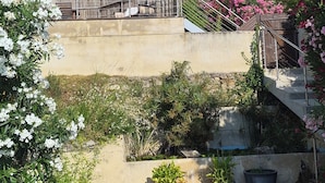 A garden with potted plants, a wooden deck, and a concrete wall. - Air-conditioned house in a fully renovated farmhouse 5' from the Ardèche. (Saint-Julien-de-Peyrolas)