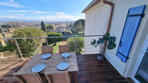 A balcony with a table set for two, wicker chairs, a potted plant, and a view of the countryside. - Air-conditioned house in a fully renovated farmhouse 5' from the Ardèche. (Saint-Julien-de-Peyrolas)