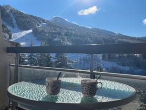 En balkon med et glasbord, to kopper og udsigt til et bjerg.