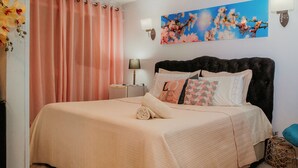 Une chambre à coucher comprenant un lit, une table de chevet, une lampe, un luminaire fixé au mur et une œuvre d’art à motifs floraux.