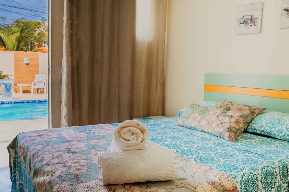 A hotel room with a bed, a view of a pool, and a window with curtains.