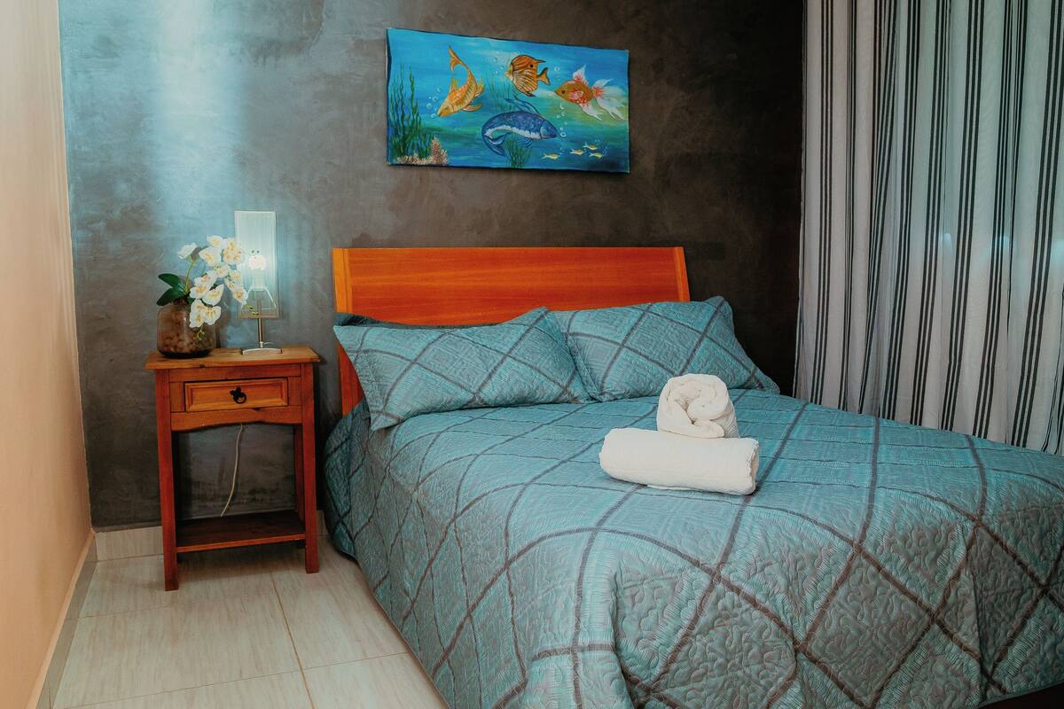 A bedroom with a bed, a nightstand, a painting, and a striped curtain.