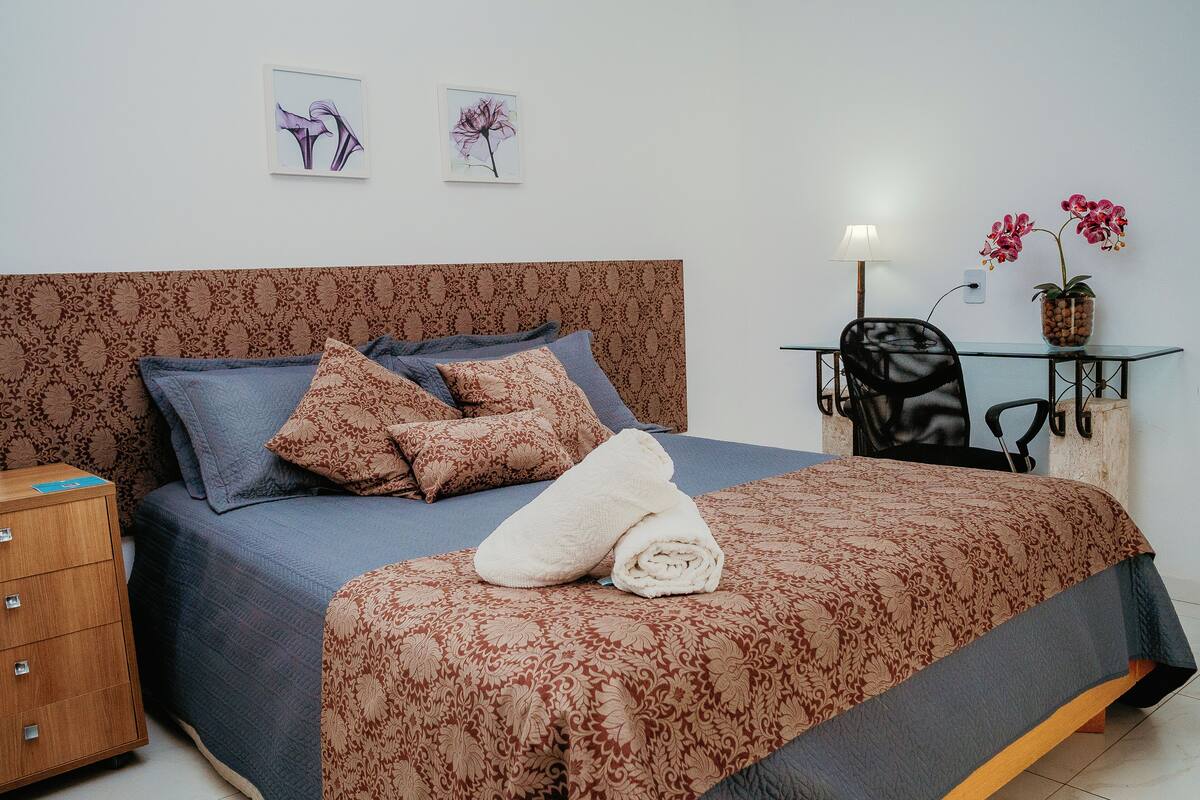 A neatly made bed with a patterned bedspread, a bedside table with a lamp, and a chair.