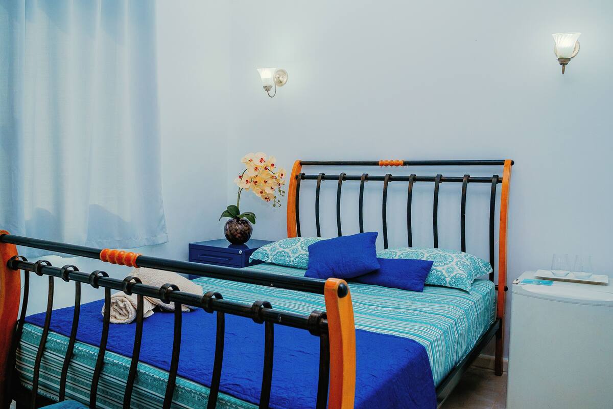 A bedroom with a bed, a nightstand, a lamp, and a window with curtains.