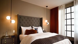 Une chambre d’hôtel moderne avec un grand lit, une tête de lit sombre, deux tables de chevet avec des lampes et une grande fenêtre avec des rideaux.