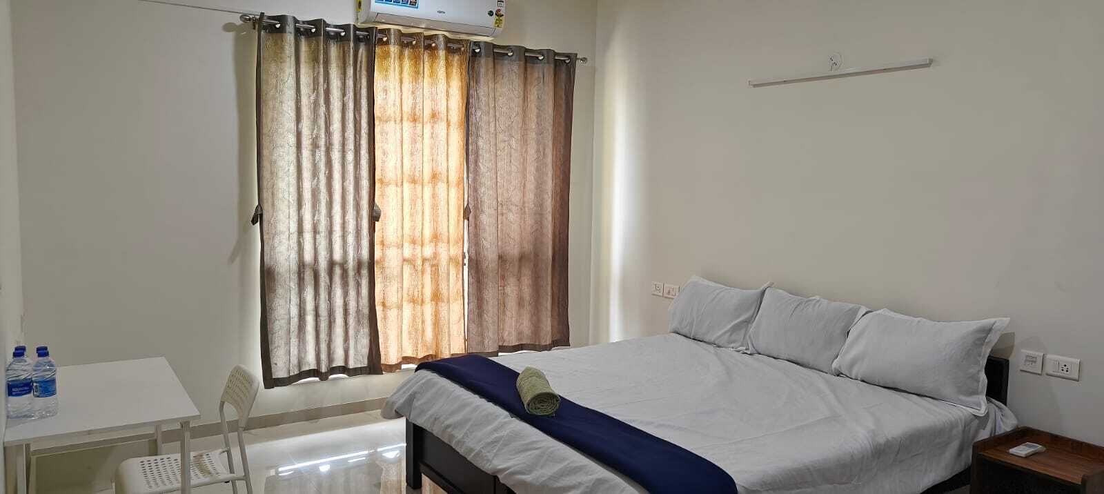 Une chambre d’hôtel avec un lit, une petite table avec des bouteilles d’eau, une chaise et une fenêtre avec des rideaux.