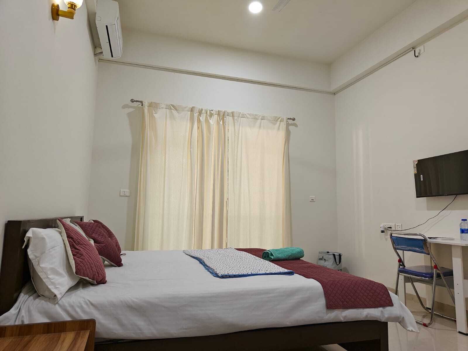 A hotel room with a bed, a desk, a chair, a TV, and a window with curtains.