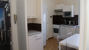A compact kitchen with white cabinets, a microwave, a stove, and a refrigerator. - Superbe T2 en Centre Ville, à 400m du Port Climatisé Avec Parking Privé (Bandol)