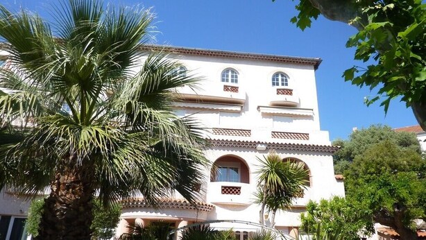 A multi-story building with a white facade, arched windows, and a tiled roof. - Superbe T2 en Centre Ville, à 400m du Port Climatisé Avec Parking Privé (Bandol)