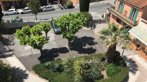 A street view with parked cars, trees, and a building with a balcony. - Superbe T2 en Centre Ville, à 400m du Port Climatisé Avec Parking Privé (Bandol)