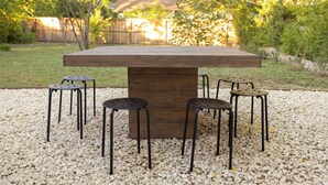 A wooden table with four black stools in a garden setting.
