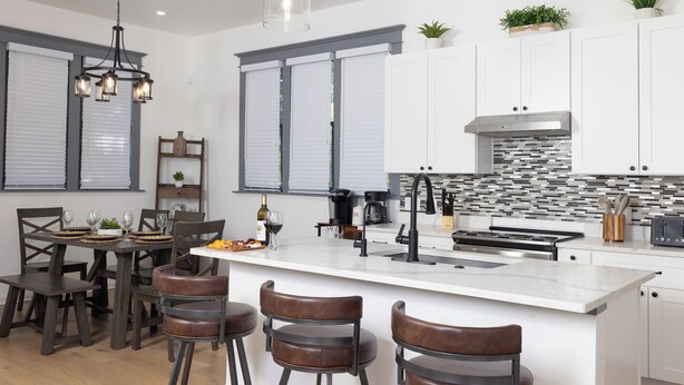 A modern kitchen with a large island, bar stools, and a dining area with a table and chairs.