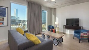 A modern living room with a grey sofa, a coffee table, a TV, and a city view. - Wyndham Resort 1BD/1BA Deluxe Suite in fantastic downtown Austin - RACE WEEKEND! (Austin)
