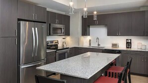 A modern kitchen with dark cabinetry, stainless steel appliances, a granite island, and red upholstered chairs. - Wyndham Resort 1BD/1BA Deluxe Suite in fantastic downtown Austin - RACE WEEKEND! (Austin)