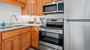 A kitchen with wooden cabinets, stainless steel appliances including a microwave, oven, and refrigerator, and a granite countertop. -  Stylish & Centrally-Located 2 bed/2 bath Condo in Auburn, AL (Auburn)