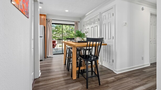 A dining area with a wooden table and chairs, a potted plant, and a view through a glass door to an outdoor space. -  Stylish & Centrally-Located 2 bed/2 bath Condo in Auburn, AL (Auburn)