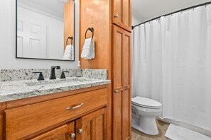 A bathroom with a wooden vanity, a mirror, a sink with a soap dispenser, and a toilet.