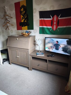 Une pièce avec un bureau en bois, un téléviseur diffusant un film, un drapeau et un mur orné d’un motif.