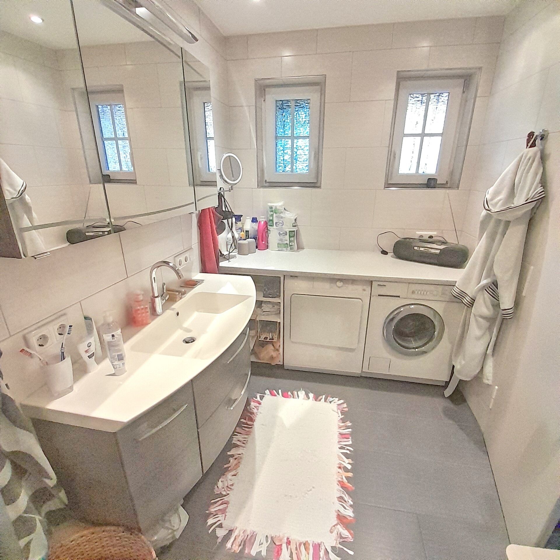 A bathroom with a sink, mirror, window, and a washing machine.