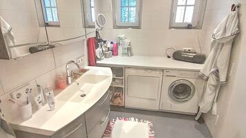 A bathroom with a sink, mirror, window, and a washing machine.