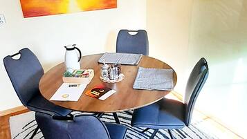 Een eetruimte met een ronde tafel, blauwe stoelen, een kroonluchter en kunstwerken aan de muren.