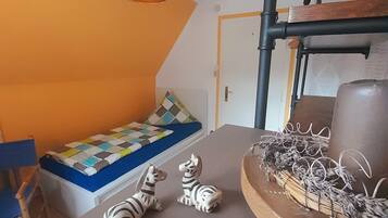 A room with a sloped ceiling, a bed with a colorful quilt, two zebra figurines, a wooden side table with a decorative item, and a white cylindrical object hanging from the ceiling.