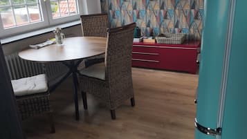 A dining area with a round table, wicker chairs, a red cabinet, and a patterned wall.