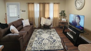 A living room with a brown leather sofa, a patterned rug, a television on a stand, and a clock on the wall.