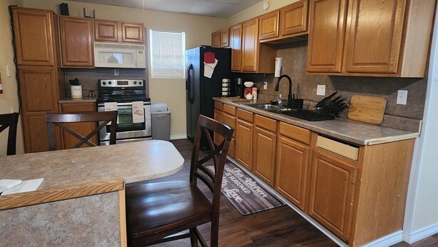 A kitchen with wooden cabinets, a microwave, a refrigerator, a stove, and a ceiling fan.