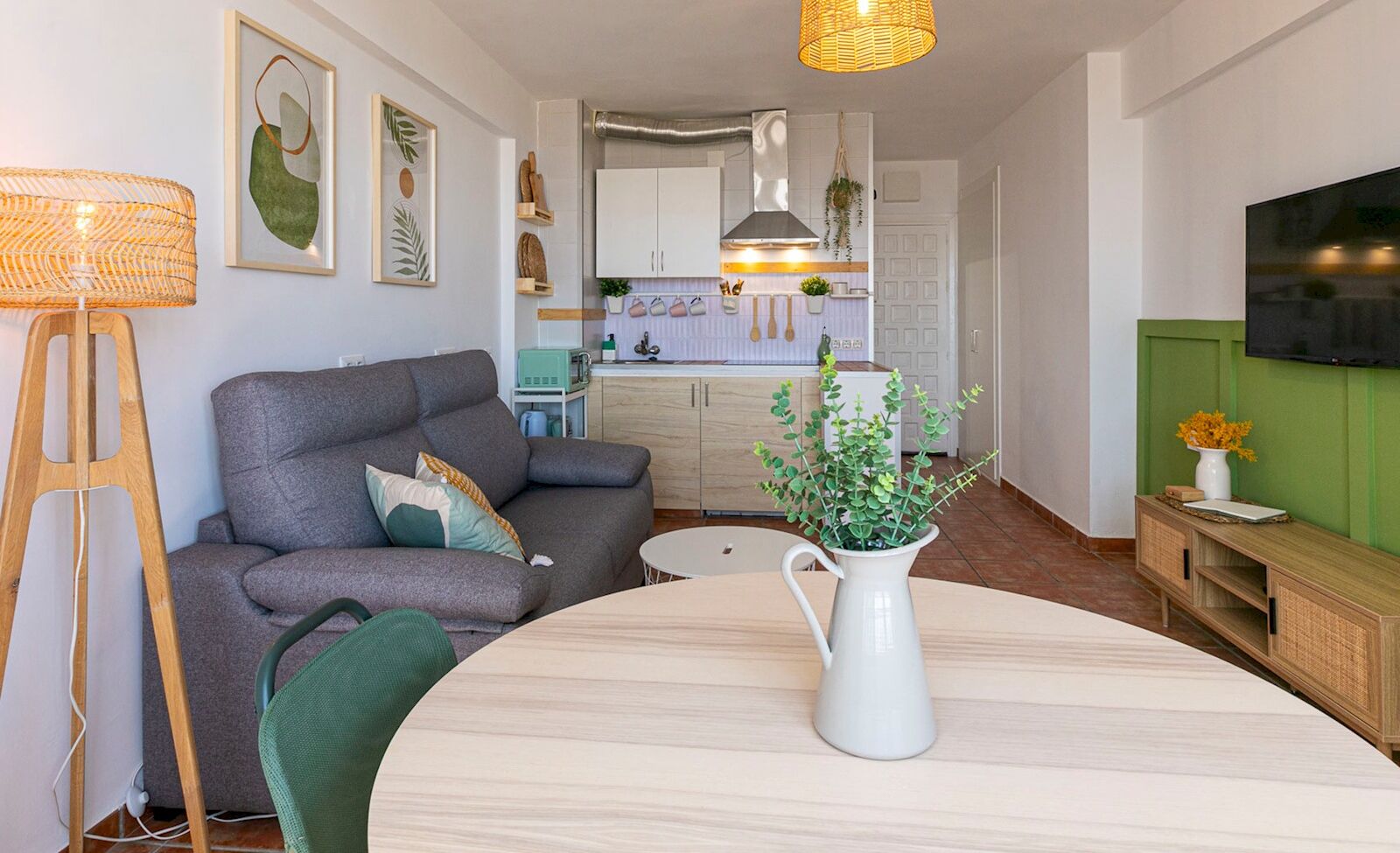 Ein modernes Wohnzimmer mit einem grauen Sofa, einem Holztisch und einer weißen Vase mit Grünpflanzen.